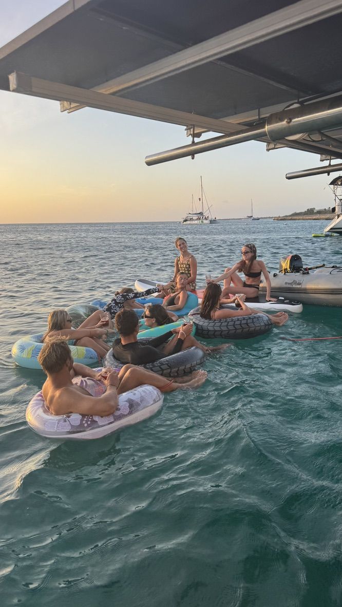 Crew lounging on floaties in the water behind Laurelli at sunset