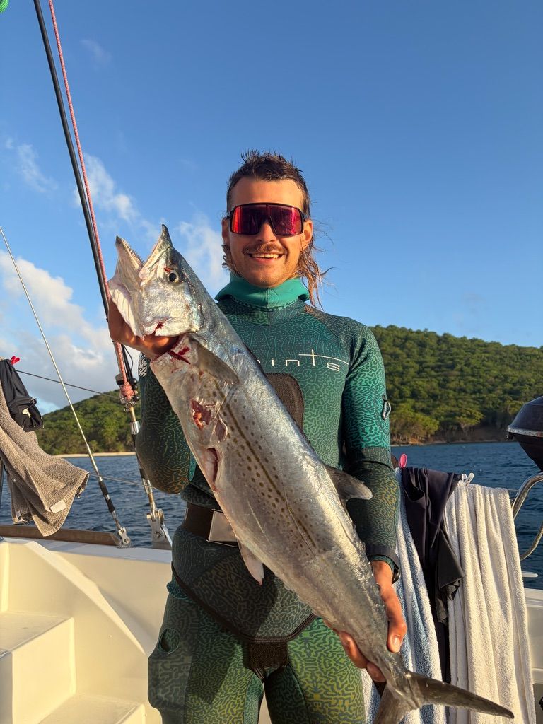 Crew member in a wetsuit holding a speared fish on deck